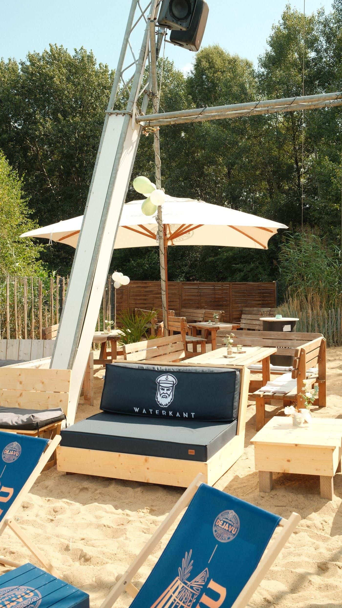 Lounge im Sand: dunkelblaues Sofa, Liegestühle und ein Sonnenschirm, Luftballons am Mast