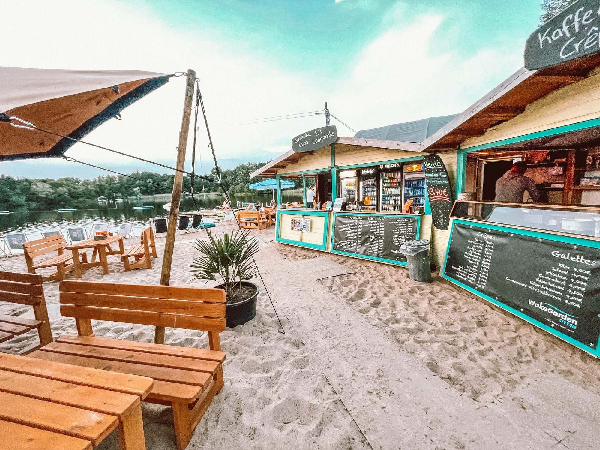 Gelb-türkise Imbisshütte am Strand mit Kreidetafeln für Crêpes und Galettes, ein Mitarbeiter an der Ausgabe